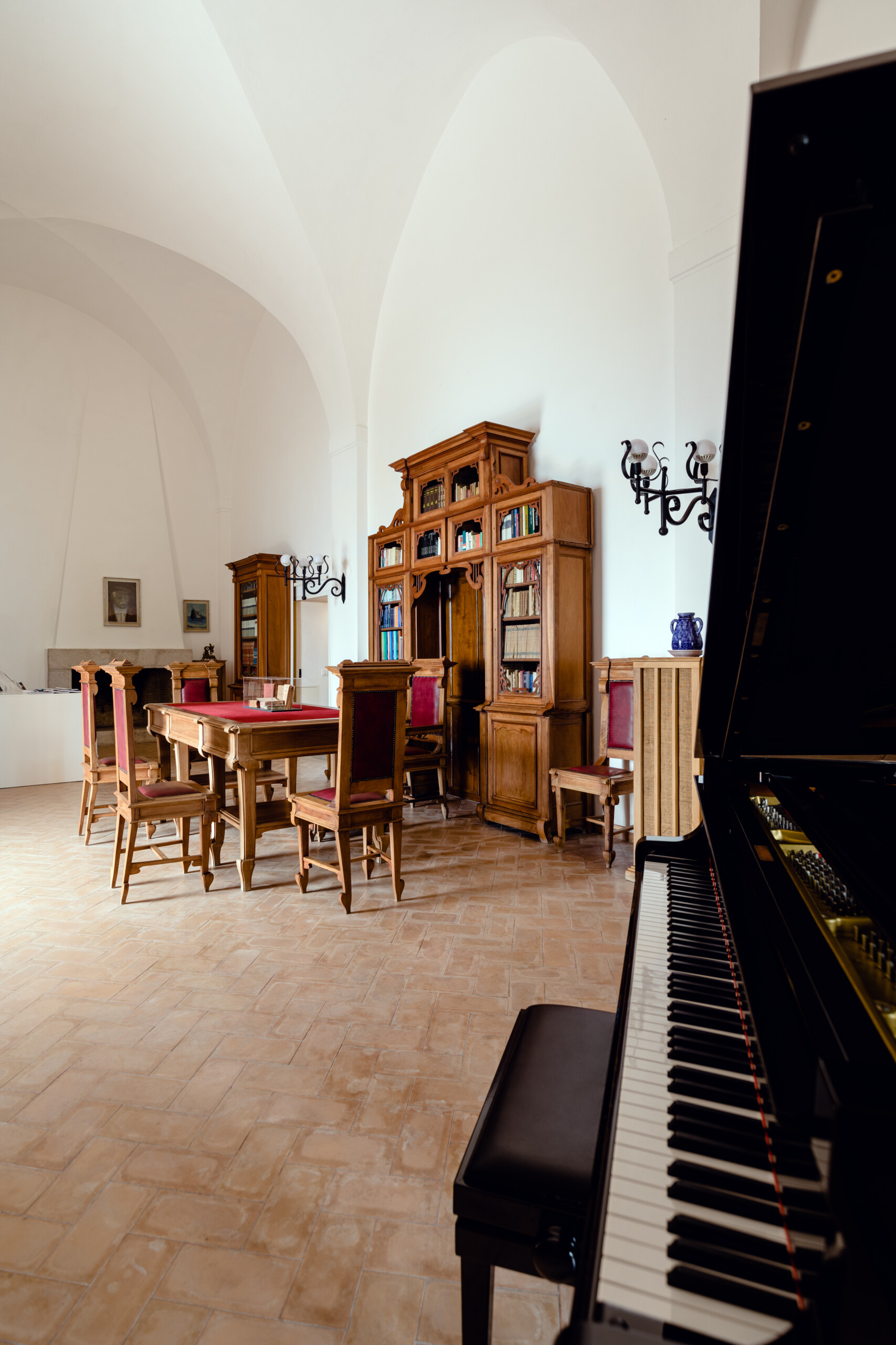 Bourbon26 (6) Grand piano along the right in a bright vaulted room with wooden bookcases and red-upholstered chairs.